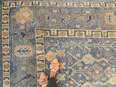 Woman standing on the corner of a blue & green Oushak Turkish area rug.
