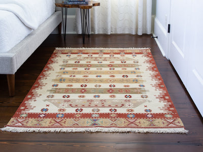 A red & orange small Turkish Kilim rug on a dark hardwood floor.