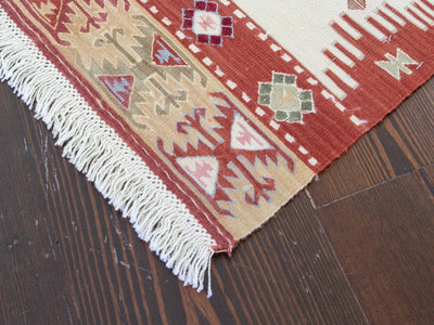 Closer of of the corner on a red & orange small Turkish Kilim rug.