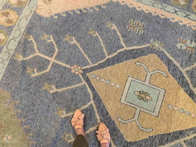 Woman in tan leather flats standing on a blue & green Oushak Turkish area rug.