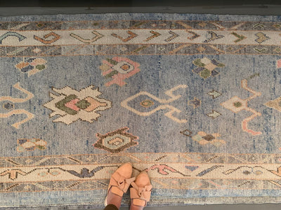 Woman in tan flats standing on a blue & green Turkish runner rug.