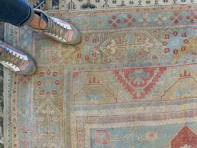 Corner shot of an extra large red & orange Sivas Turkish Rug with a set of feet.