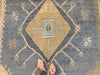 Woman in tan flats standing over central medallion on a blue & green Oushak Turkish area rug.