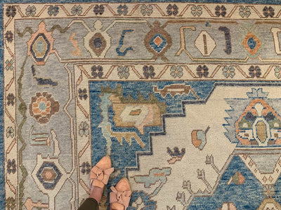 Woman in tan slides standing over the corner medallion on a blue & green Oushak Turkish area rug.