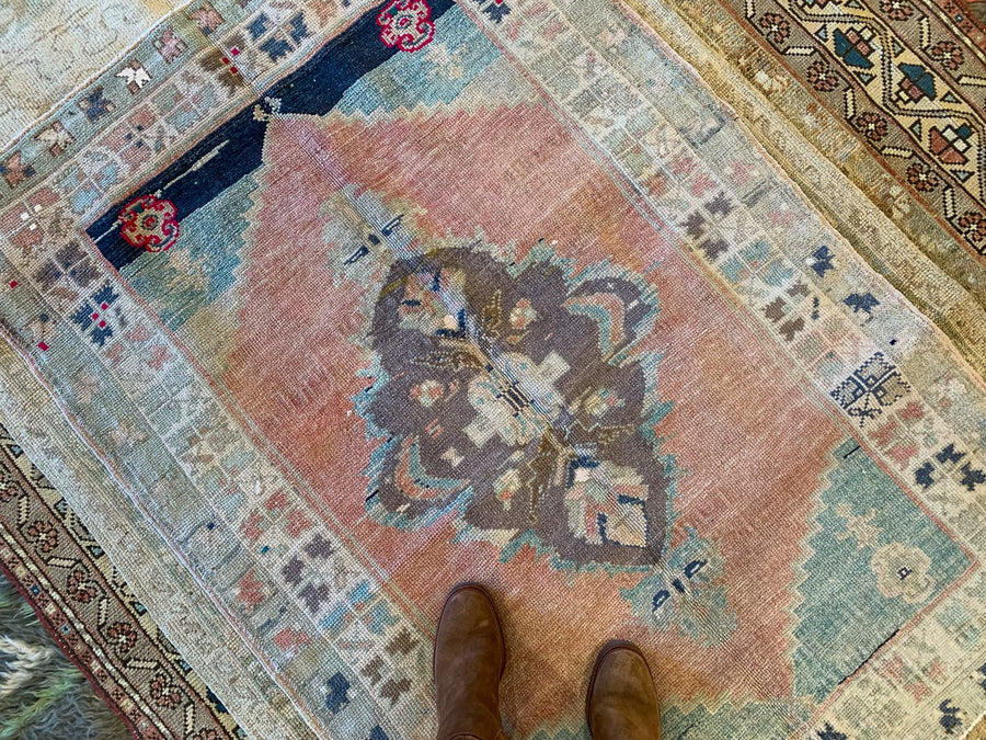 Woman in riding boots standing on a small blue & green Sivas Turkish rug.