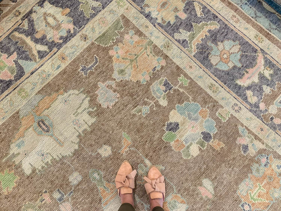 Woman in tan leather flats standing on a brown & grey Oushak Turkish area rug.
