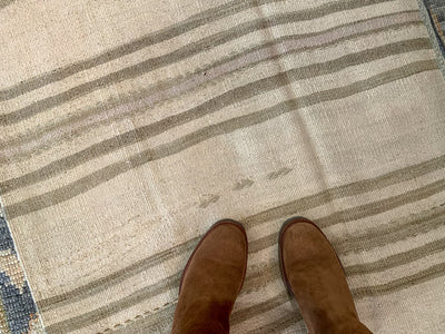 Woman in riding boots standing on a brown & grey Turkish rug runner.