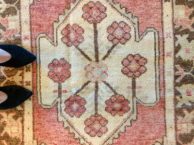 Woman in heels standing next to the central medallion on a small red & orange Cal Turkish rug.