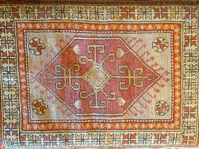 Top down view of a small red & orange Yuntdag Turkish rug.